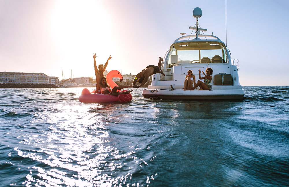 Group of friends enjoying a summer day on a inflatable toy and yacht. Young people having fun. Man diving in the sea with friends cheering from yacht and inflatable toy.